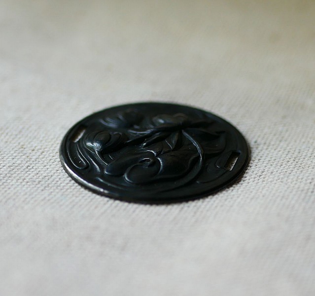 Vannliljemedaljong i svart metallrelieff med sideb&aring;nd 